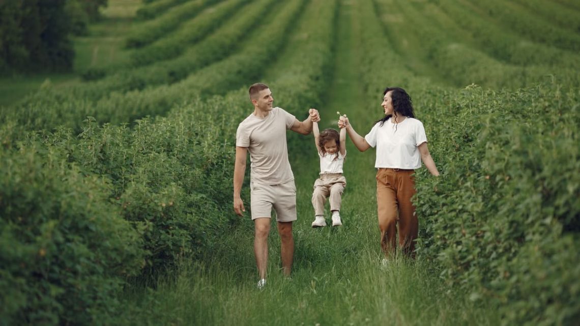 A happy family walking in a lush, green rural field together.