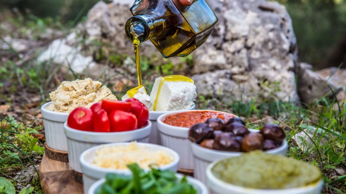 Outdoor picnic with various Mediterranean spreads, herbs, and olive oil drizzle.