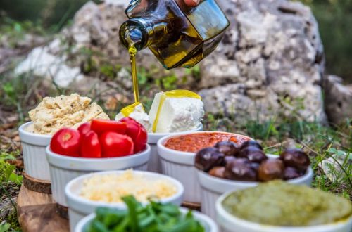Outdoor picnic with various Mediterranean spreads, herbs, and olive oil drizzle.